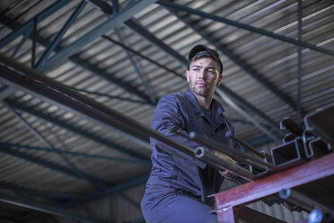 Mechaniker in der Werkstatt, der eine Stahlstange von einem Hochregal nimmt - ZEF009294
