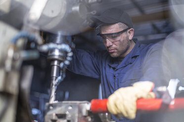 Mechaniker mit Schutzbrille an einer Bohrmaschine in einer Werkstatt - ZEF009297