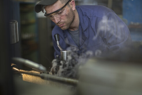 Mechaniker mit Schutzbrille an einer Maschine in der Werkstatt - ZEF009314