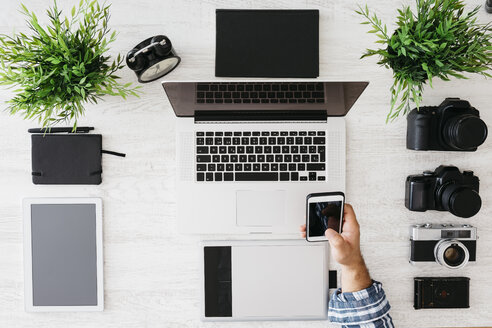 Fotograf bei der Arbeit am Schreibtisch mit Smartphone, Teilansicht - JRFF000775