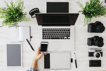 Fotograf bei der Arbeit am Schreibtisch mit Smartphone, Teilansicht - JRFF000778