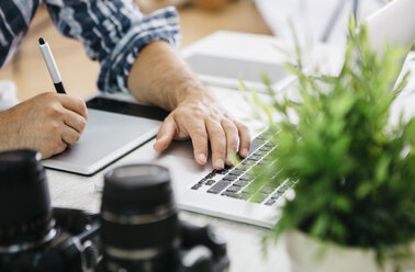 Fotograf bei der Arbeit am Schreibtisch mit Grafiktablett, Teilansicht - JRFF000781