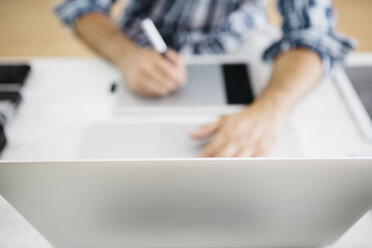 Man working at desk with laptop and graphic tablets, partial view - JRFF000782