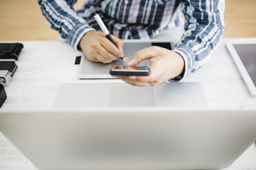 Photographer working at desk with graphics tablet and smartphone, partial view - JRFF000783