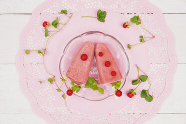 Homemade wild strawberry ice lollies on glass plate and pink cake lace - GWF004860