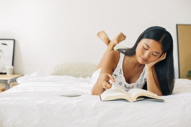 Young woman lying in bed reading book - EBSF001558