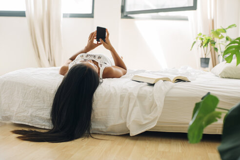 Junge Frau liegt im Bett und benutzt ein Mobiltelefon - EBSF001565