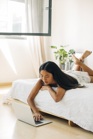 Junge Frau im Bett liegend mit Laptop, lizenzfreies Stockfoto