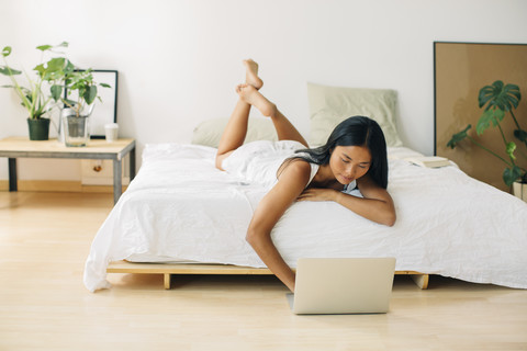 Junge Frau im Bett liegend mit Laptop, lizenzfreies Stockfoto