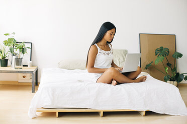 Junge Frau sitzt auf dem Bett und benutzt einen Laptop - EBSF001568
