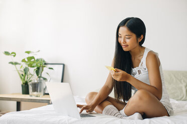 Junge Frau sitzt auf dem Bett und kauft online ein - EBSF001574