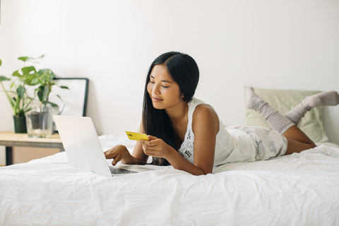 Junge Frau liegt im Bett und kauft online ein, lizenzfreies Stockfoto