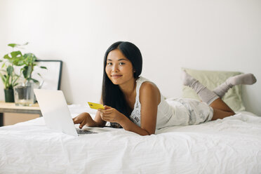 Junge Frau liegt im Bett und kauft online ein - EBSF001577
