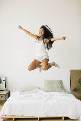 Übermütige junge Frau springt auf dem Bett, lizenzfreies Stockfoto