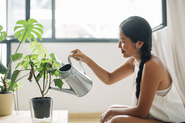 Young woman at home watering plant - EBSF001599