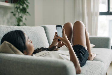 Young woman lying on couch using cell phone - EBSF001604