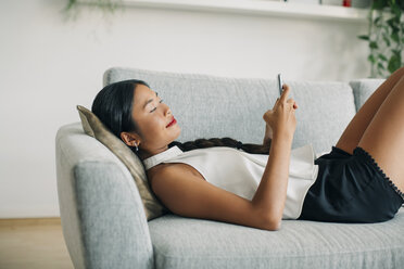 Junge Frau liegt auf der Couch und benutzt ein Mobiltelefon - EBSF001605