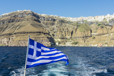 Griechenland, Santorini, griechische Flagge mit Fira im Hintergrund von der Caldera aus gesehen - THAF001715