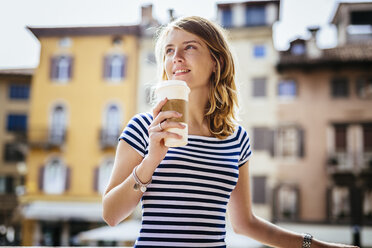 Italien, Udine, Porträt einer lächelnden jungen Frau mit Kaffee zum Mitnehmen - GIOF001334