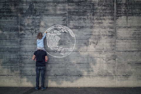 Österreich, Salzburg, Vater mit Tochter auf den Schultern, die Tochter zeichnet mit Kreide die Erde auf eine Betonwand, lizenzfreies Stockfoto