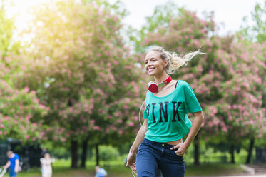 Glückliche blonde Frau mit Kopfhörern beim Spaziergang in einem Park - DIGF000824