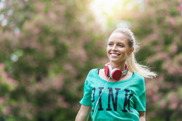 Porträt einer glücklichen blonden Frau mit Kopfhörern in einem Park - DIGF000825