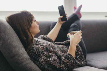 Junge Frau entspannt sich auf der Couch mit einer Tasse Kaffee und macht ein Selfie mit ihrem Smartphone - LCUF000027