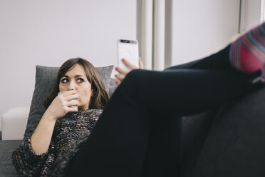 Junge Frau entspannt sich auf der Couch mit einer Tasse Kaffee und macht ein Selfie mit ihrem Smartphone - LCUF000028