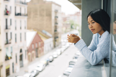 Young woman with cup of coffee leaning out of window - EBSF001626