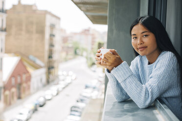 Young woman with cup of coffee leaning out of window - EBSF001627