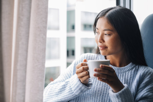 Junge Frau mit einer Tasse Kaffee vor einem offenen Fenster stehend - EBSF001632