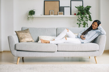 Junge Frau entspannt sich auf der Couch im Wohnzimmer und benutzt ihr Smartphone - EBSF001640
