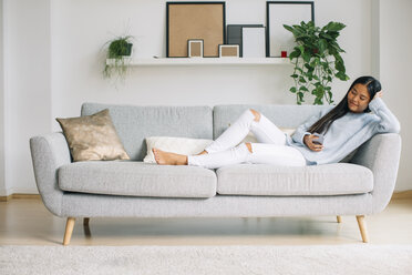 Young woman relaxing on couch in the living room using smartphone - EBSF001640