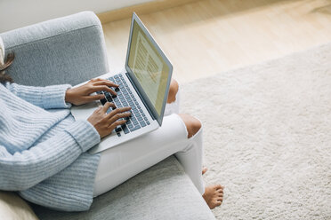 Junge Frau sitzt zu Hause auf der Couch und benutzt einen Laptop, Teilansicht - EBSF001646