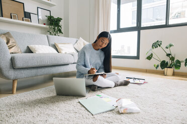 Young woman sitting on floor in the living room writing down something - EBSF001657