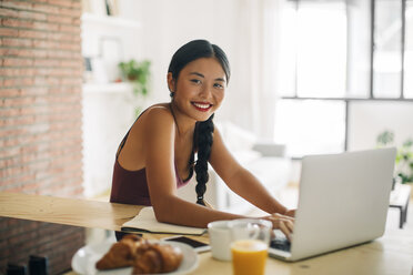 Porträt einer lächelnden Frau, die zu Hause mit einem Laptop arbeitet - EBSF001665