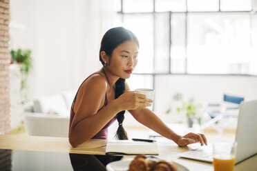 Frau mit einer Tasse Kaffee bei der Arbeit mit dem Laptop zu Hause - EBSF001666