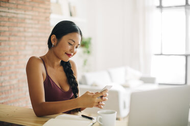 Lächelnde Frau schaut auf ihr Handy zu Hause - EBSF001668