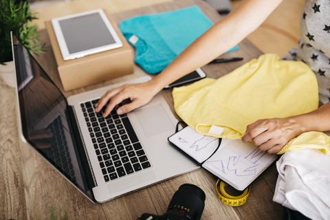 Frau mit Kleidungsstück und Laptop auf dem Schreibtisch, lizenzfreies Stockfoto