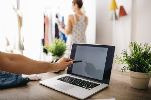 Mann zeigt auf Laptop mit Frau im Hintergrund, lizenzfreies Stockfoto