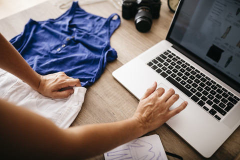 Frau mit Kleidungsstück und Laptop auf dem Schreibtisch, lizenzfreies Stockfoto