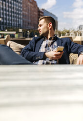 Junger Mann wartet in einem Straßencafé und beobachtet etwas - MGOF002115