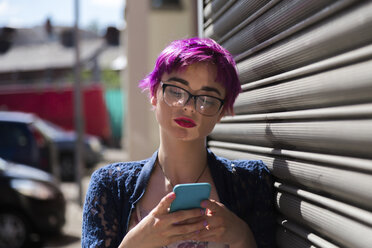 Porträt einer jungen Frau mit gefärbtem Haar, die auf ihr Mobiltelefon schaut - BOYF000460