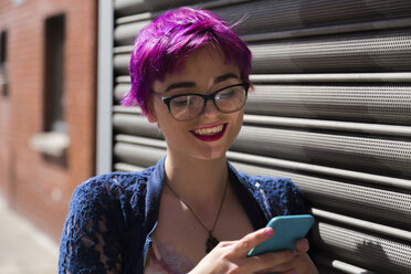 Porträt einer lächelnden jungen Frau mit gefärbtem Haar, die auf ihr Mobiltelefon schaut - BOYF000461