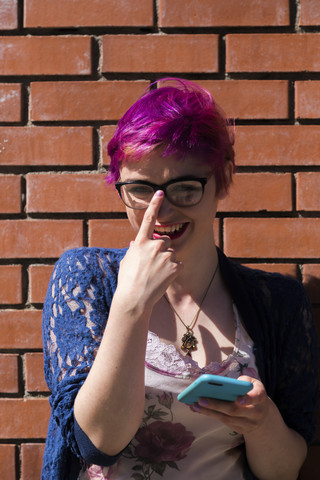 Porträt einer lachenden jungen Frau mit gefärbtem Haar, die ihre Brille zurechtrückt, lizenzfreies Stockfoto