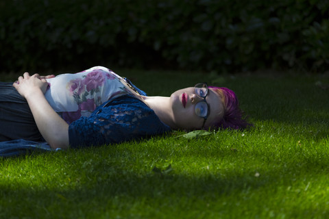 Porträt einer entspannten jungen Frau mit gefärbtem Haar, die auf einer Wiese liegt, lizenzfreies Stockfoto