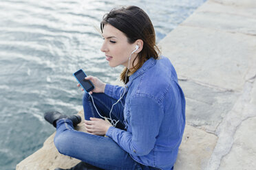 Young woman sitting on dock listening to music - BOYF000475