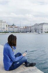 Italien, Triest, junge Frau sitzt auf dem Steg und hört Musik - BOYF000476