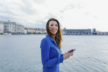 Italien, Triest, lächelnde junge Frau, die am Hafen Musik hört - BOYF000478