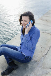 Smiling young woman sitting on dock talking on cell phone - BOYF000480